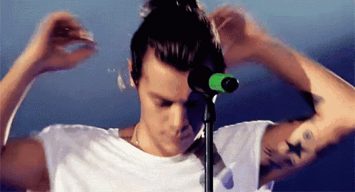 a man in a white shirt is standing in front of a microphone and tying his hair in a bun .