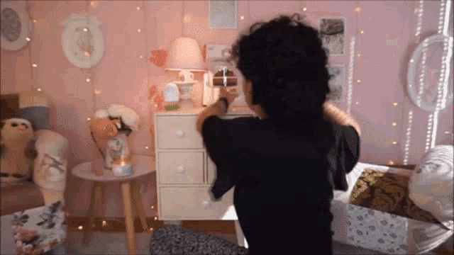 a woman in a black shirt is standing in front of a dresser in a pink room
