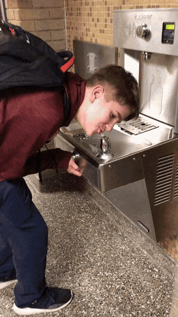 a boy is drinking from a water fountain that says kenwood on it