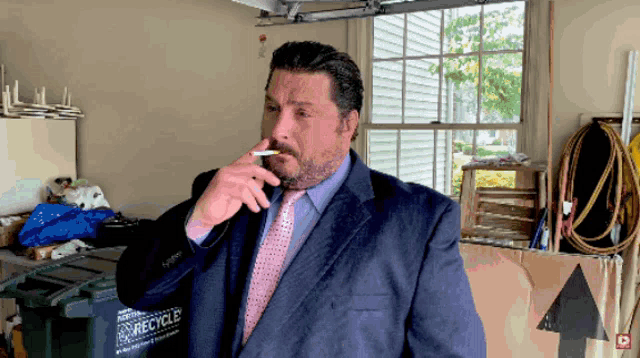 a man in a suit and tie smoking a cigarette in front of a recycle bin