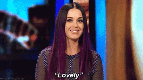 a woman with purple hair is smiling and saying `` lovely '' while sitting on a stage .