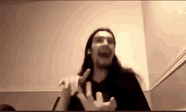 a man with long hair and a beard is making a funny face while sitting in front of a computer screen .
