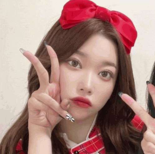 a girl wearing a red bow on her head is giving a peace sign
