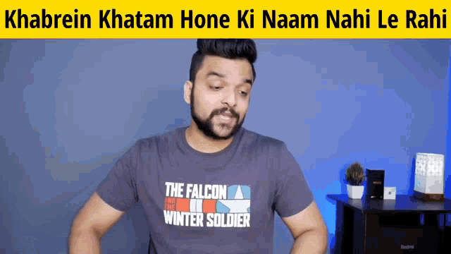 a man wearing a falcon winter soldier t-shirt stands in front of a blue wall