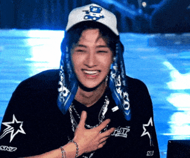 a young man wearing a hat and a scarf is smiling and holding his chest .