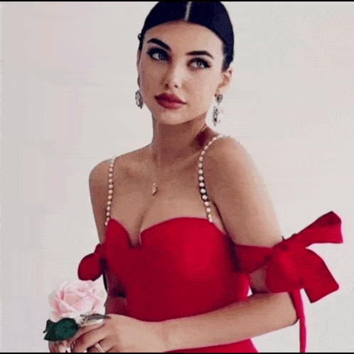 a woman in a red dress with pearls on the straps is holding a rose .