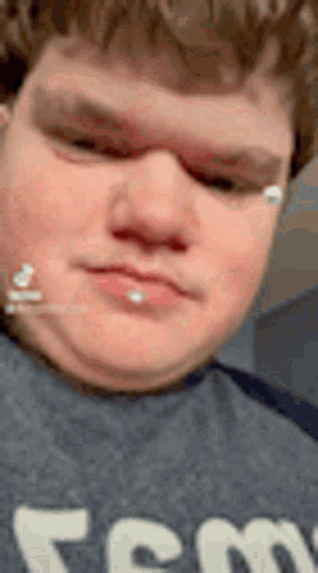 a close up of a man 's face with a piercing in his lip and a gray shirt .