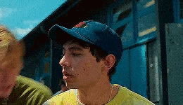 a man wearing a blue baseball cap and a yellow shirt is standing in front of a blue building .