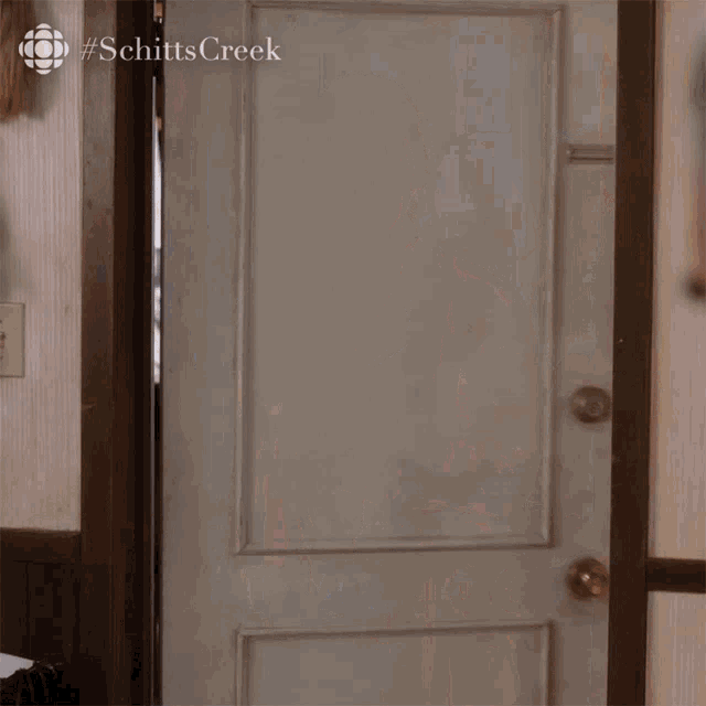 a woman in a bathrobe is opening a door with the hashtag schitts creek on the bottom