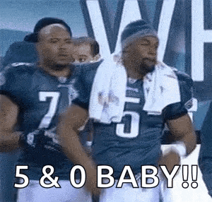 two football players are standing next to each other on a field and one of them is holding a baby .