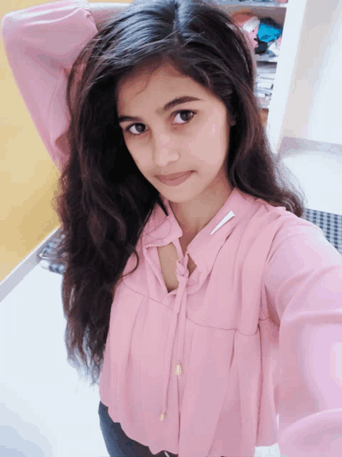 a woman in a pink shirt is taking a selfie with her hand in her hair