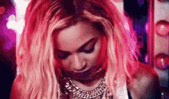 a woman with pink hair is wearing a necklace and looking down at something .