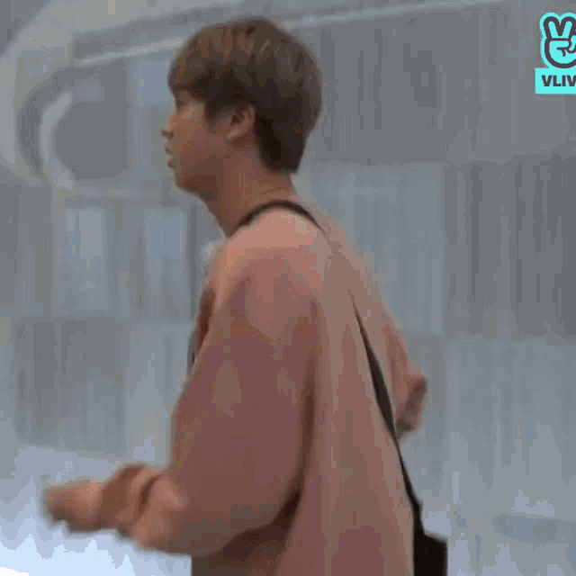 a young man in a pink sweater is walking with a black bag .