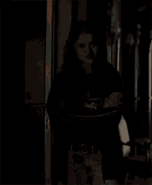 a young woman is standing in a dark room with her arms crossed and smiling .