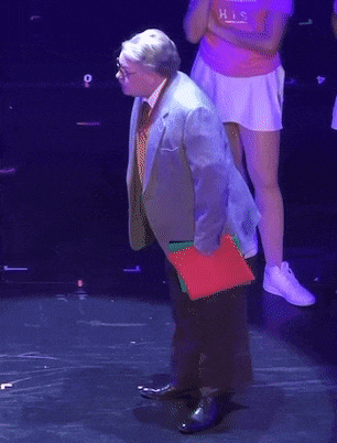 a man stands on a stage holding a red folder that says his on it