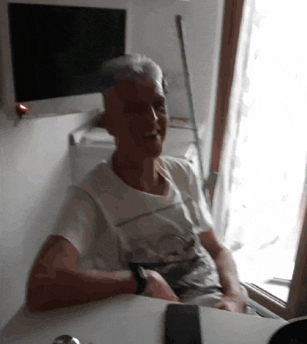 a man in a white shirt is sitting at a table with a phone on it