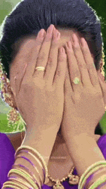 a woman is covering her face with her hands while wearing bracelets and a ring .