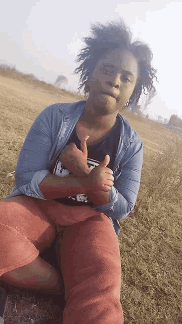 a woman sitting in a field giving a thumbs up sign