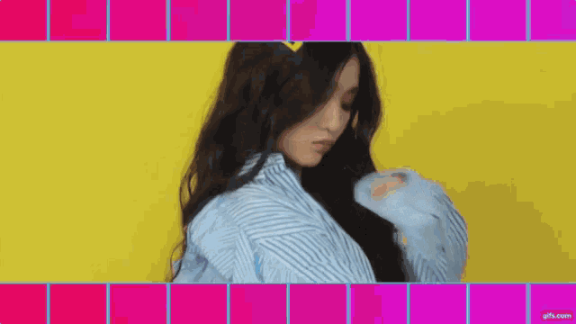 a woman in a blue and white striped shirt is standing in front of a yellow and pink background .