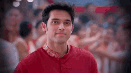 a man in a red shirt is standing in front of a crowd and smiling .