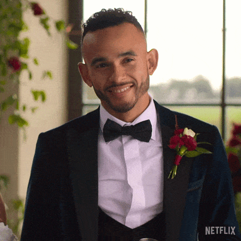 a man in a tuxedo with a bow tie is smiling in front of a netflix logo .