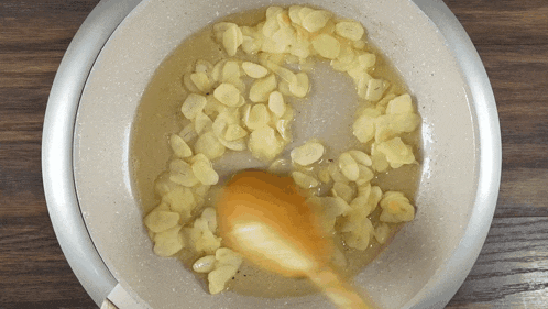 a wooden spoon is stirring sliced garlic in a frying pan