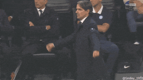 a man in a suit and tie holds his fist in the air while watching a sports game on sky sport