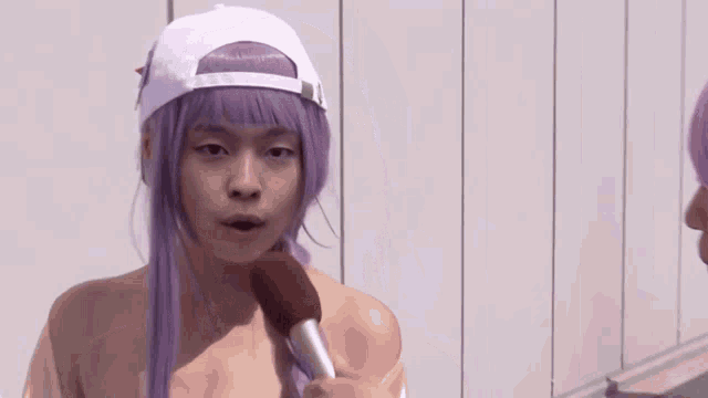 a woman with purple hair is wearing a white hat and talking into a microphone