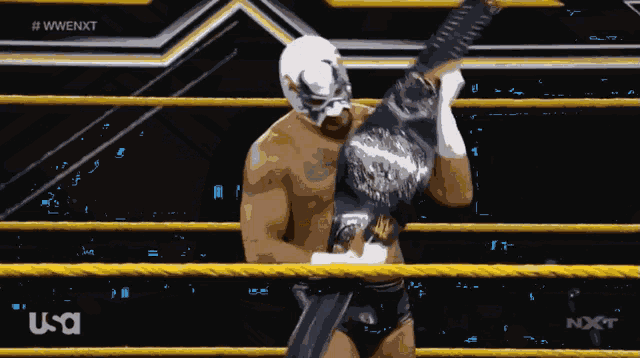 a man in a mask is holding a wrestling belt in a ring
