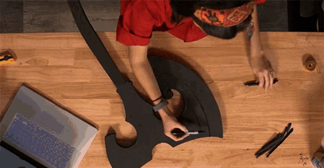a person is drawing on a piece of foam on a wooden table next to a laptop