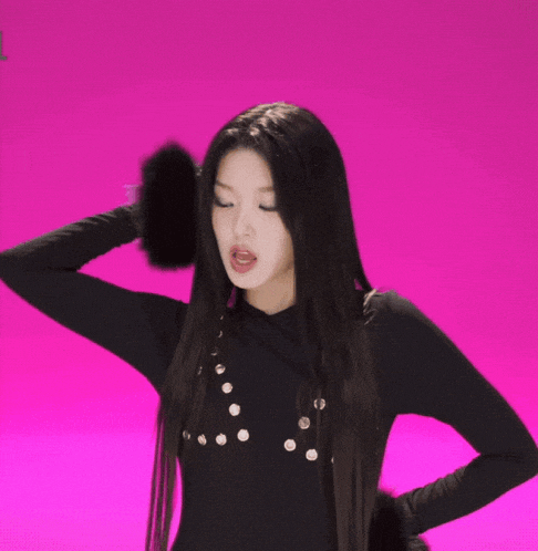 a woman in a black top holds her hair in a ponytail on a pink background