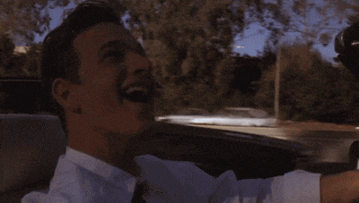 a man in a white shirt and tie laughs while driving a car