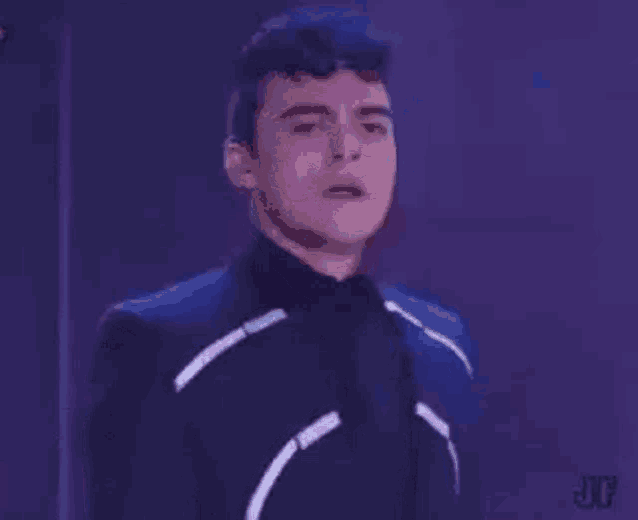 a young man in a suit is standing in front of a neon light .