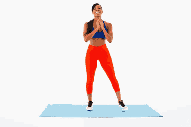 a woman in orange pants and a blue top is standing on a blue mat