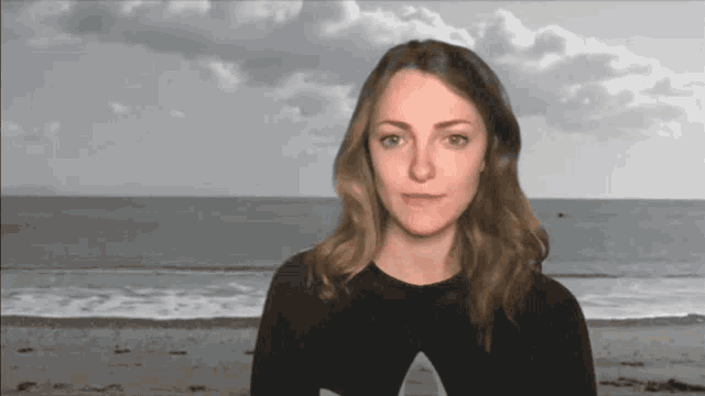 a woman wearing a black shirt with an a on it stands in front of the ocean