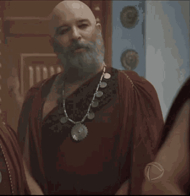a bald man with a beard is wearing a red robe and necklace