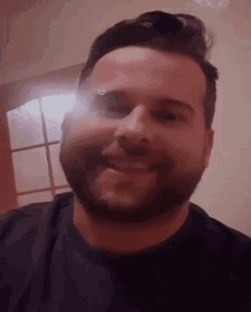 a man with a beard is smiling for the camera while wearing a black shirt .