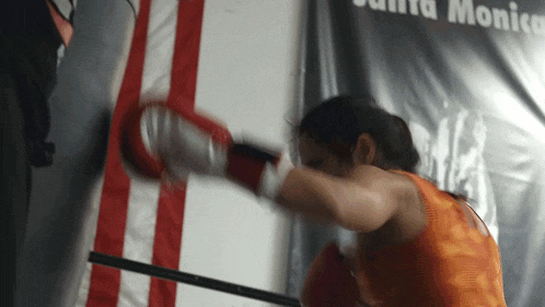 a woman wearing boxing gloves is hitting a punching bag in front of a santa monica banner