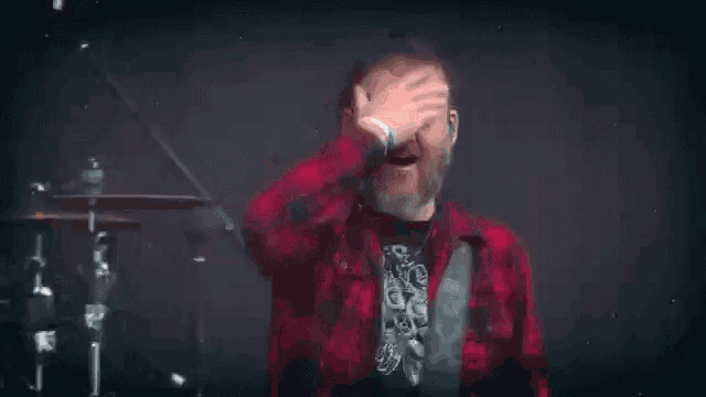 a man in a red plaid shirt is covering his eyes with his hand