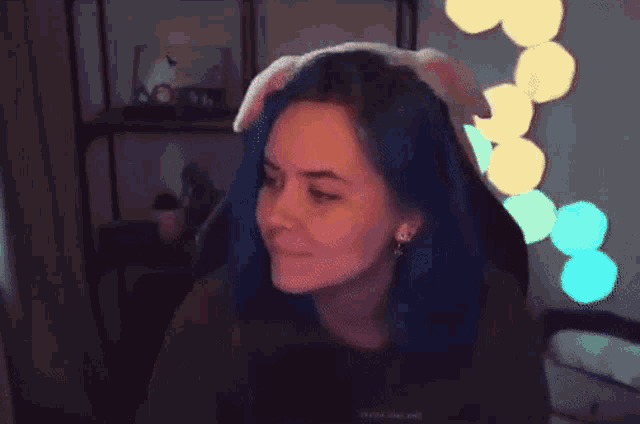 a girl with blue hair is sitting in a chair with a stuffed bunny hat on her head