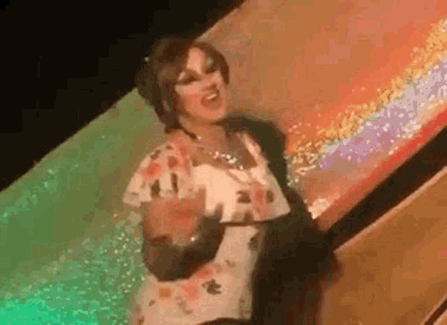a woman in a floral dress is dancing on a stage in front of a colorful background .