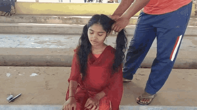 a woman in a red dress is being braided by a man in blue pants