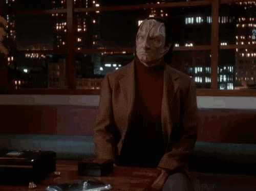 a man with a mask on his face is sitting at a table with the words so written on it