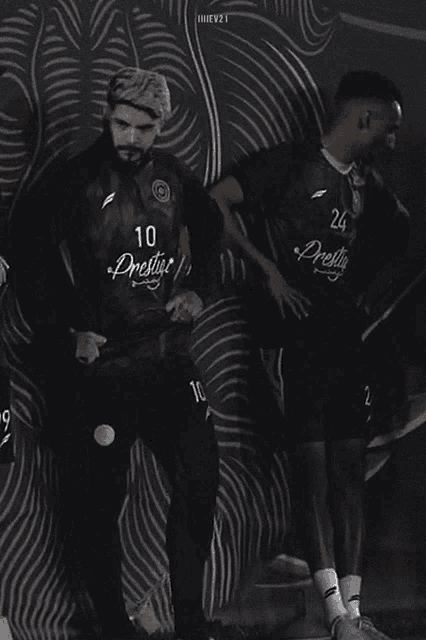 a man in a black jersey with the number 10 on it stands next to another man in a black jersey with the number 24 on it