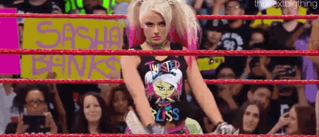 a female wrestler is standing in a wrestling ring in front of a crowd .