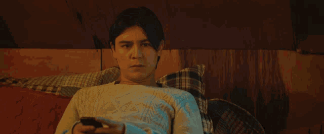 a man in a white sweater is laying on a bed holding a cell phone