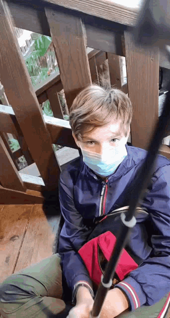 a young boy wearing a face mask is sitting on a wooden deck