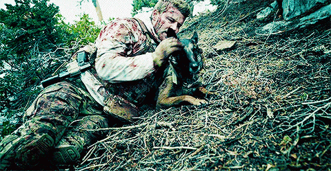a soldier is laying on the ground with a dog .