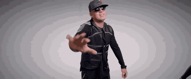 a man wearing sunglasses and a hat with the letter t on it reaches out his hand