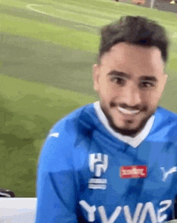 a man with a beard is wearing a blue jersey and smiling .